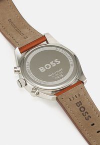 Orologio in acciaio inossidabile con cinturino in pelle marrone. Il retro presenta dettagli incisi tra cui "BOSS" e indicazioni di resistenza all'acqua.