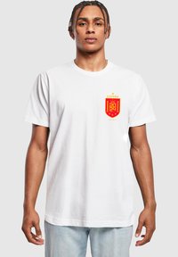 Hvid bomulds T-shirt med et rødt Spanien våbenskjold med gyldne detaljer på venstre bryst. Korte ærmer og et klassisk rund halsudskæring design.