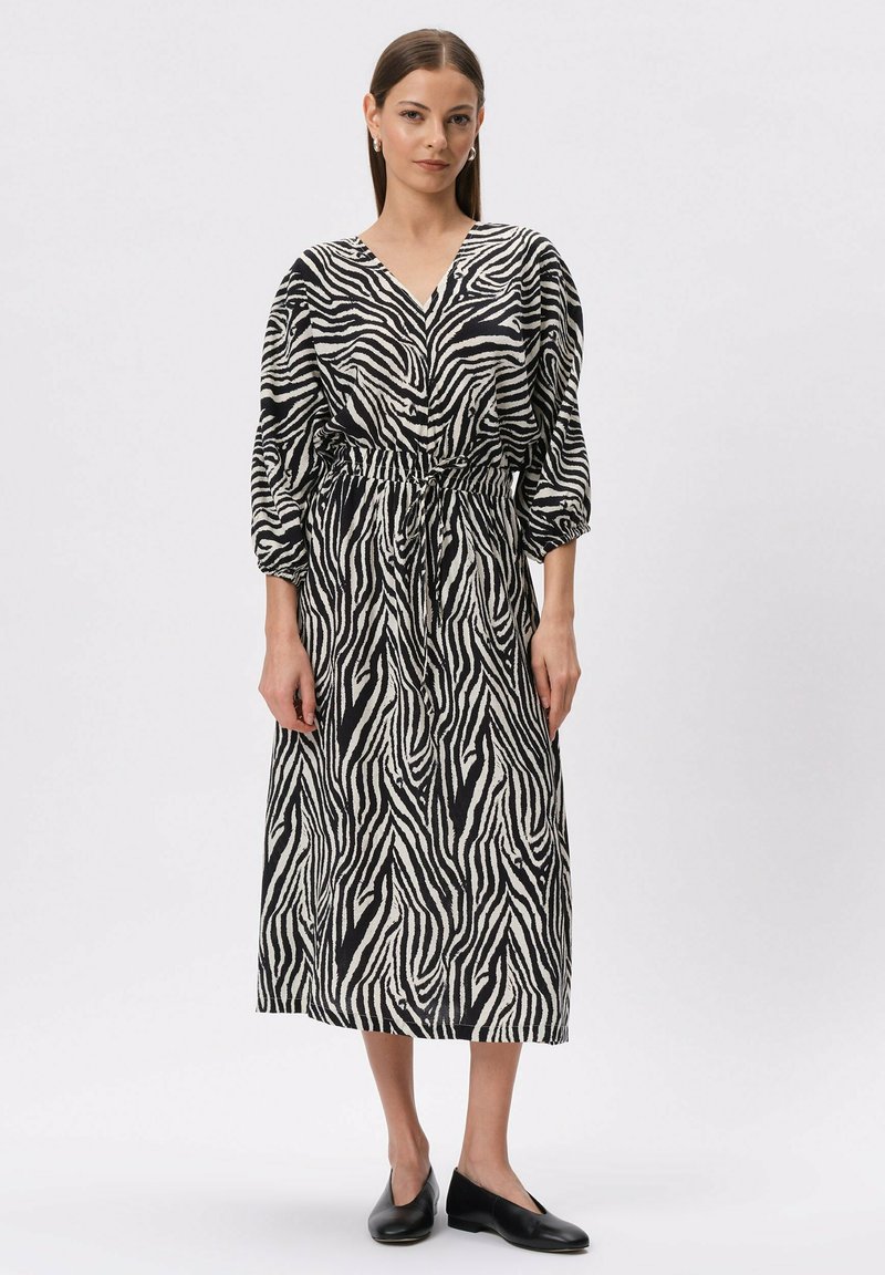 Sukienka w czarno-białe paski zebry z dekoltem w kształcie litery V, długimi bufkami oraz regulowanym paskiem w talii, wykonana z lekkiego materiału.