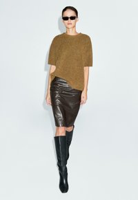Maglione lavorato a maglia marrone chiaro, gonna a matita in pelle marrone scuro e stivali neri alti fino al ginocchio. Modella con occhiali da sole neri, design minimalista.