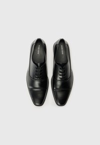 Chaussures habillées noires en cuir avec une texture lisse, un nez pointu et un design à lacets ; présentant une couture subtile sur le dessus.