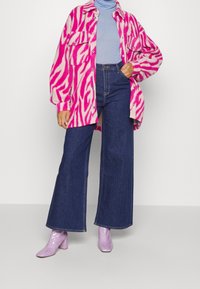 Överdimensionerad skjorta-jacka med zebramönster i rosa och kräm, över en ljusblå polotröja, i kombination med mörkblå vida jeans och lavendelfärgade ankelstövlar.