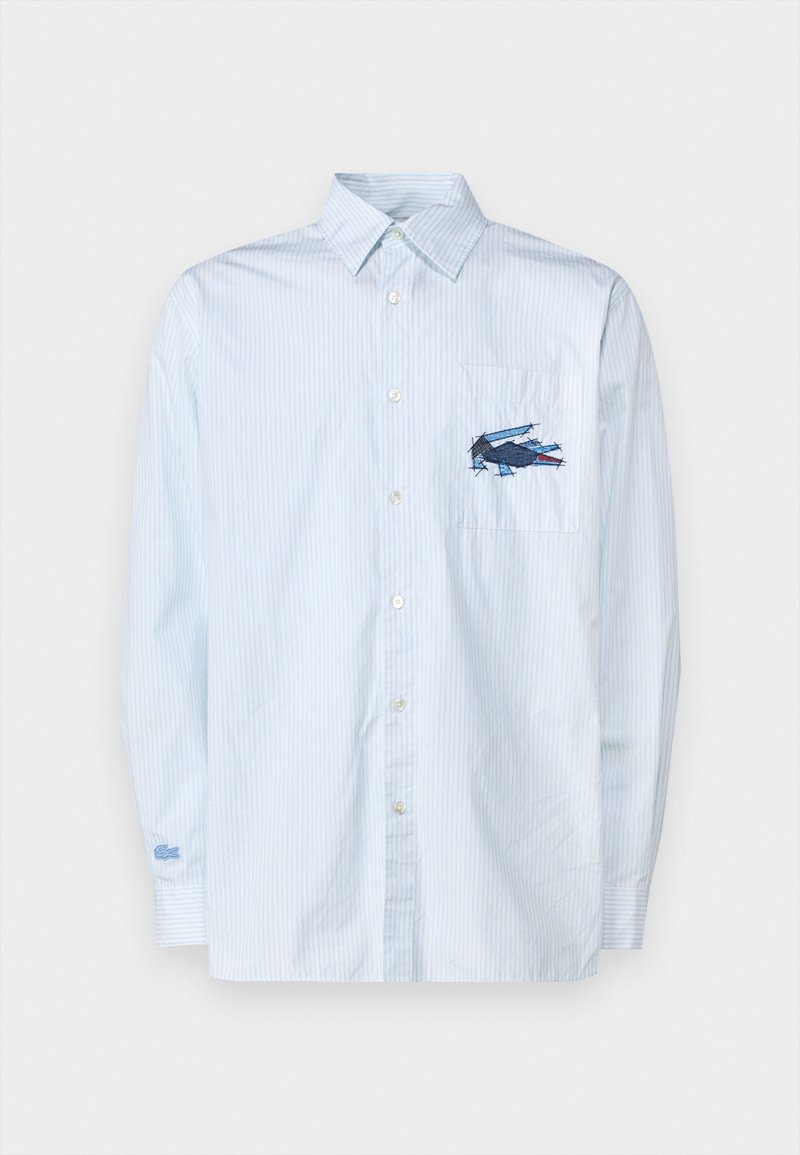 Camicia button-up a righe blu chiaro, con taschino sul petto decorato da un design blu ricamato. Maniche lunghe con polsini abbottonati.