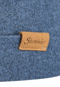 Woolen blue hat with a textured surface, featuring a tan leather label sewn into the fabric, displaying the word "Stentaler."