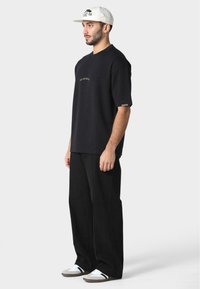 Black cotton t-shirt with short sleeves and gold text, paired with straight-leg black pants and white sneakers with grey accents.