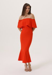 Rochie roșie fără umeri, cu un guler stratificat cu volane. Siluetă ajustată care se lărgește la tiv. țesătură netedă și detalii de design simple.