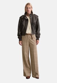 Braune Lederbomberjacke mit Rippbündchen, cremefarbenem Oberteil und karottenförmigen, weiten Hosen in Beige- und Brauntönen. Braune Ankle Boots.