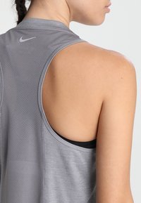 Acercamiento al hombro y parte superior de la espalda de una persona vestida con una camiseta deportiva sin mangas de Nike de color gris, con el logo de Nike visible.