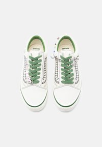 Baskets en toile blanches avec des lacets et des accents verts. Caractérisées par des détails cousus et des perles décoratives sur les lacets. Semelle plate.