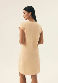 Sukienka na krótki rękaw, do kolan, z miękkiego materiału w odcieniu brzoskwiniowym, z okrągłym dekoltem i swobodnym krojem oraz bocznymi rozcięciami dla wygody ruchu.