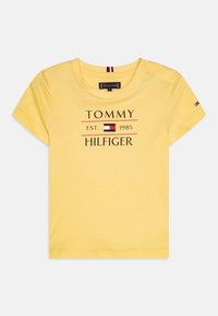 Żółta bawełniana koszulka z krótkim rękawem, okrągłym dekoltem i nadrukowanym logo "TOMMY HILFIGER EST. 1985" z czerwonymi i czarnymi akcentami.