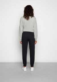 Felpa grigia con scollo rotondo, abbinata a pantaloni joggers neri a sigaretta e sneaker bianche, vista da dietro su uno sfondo neutro.