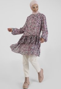 Floral-patterned, sheer long-sleeve dress in pink and purple, with a frilled hem; paired with beige pants and light brown lace-up boots.