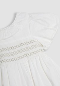 Vestido de algodón blanco con escote con volantes, mangas abullonadas y smocking decorativo con costuras plateadas en el torso.
