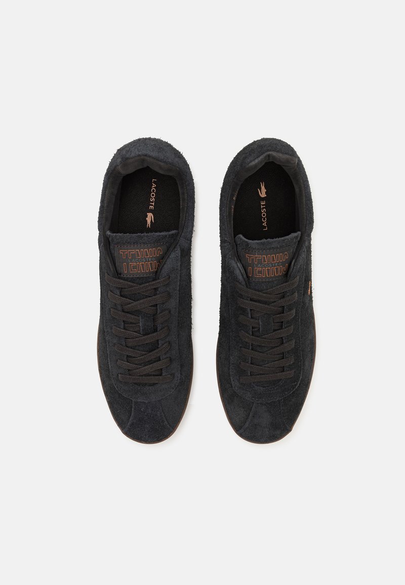 Sneakers neri in suede con lacci scuri e suola marrone. Presentano un design semplice, una tomaia testurizzata e un logo del marchio ben visibile sulla soletta.