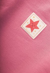 Tela rosa con un parche cuadrado cosido que muestra una estrella roja sonriente rodeada de pequeñas estrellas amarillas.