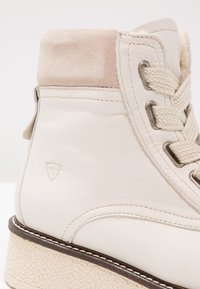 Białe skórzane botki za kostkę z zamszowym kołnierzem, okrągłymi sznurówkami i teksturowaną gumową podeszwą z lekką platformą. Subtelne logo z boku.