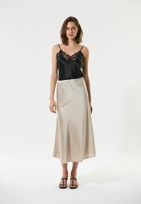 Camisola nera di satin con dettagli in pizzo, abbinata a una gonna di satin beige fluida. La modella indossa sandali neri con cinturini. Texture lisce e morbide.