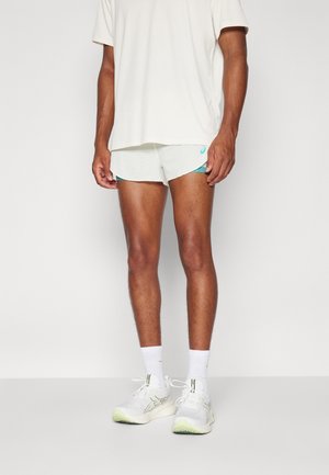 Mand iført hvide løbesko, hvide sokker, hvide sportsshorts med turkis kant og en løs hvid T-shirt.