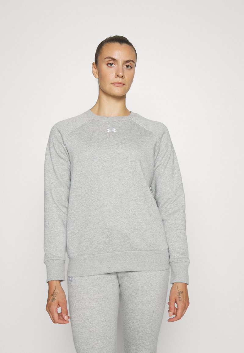 Sudadera gris con cuello redondo y mangas raglán. Fabricada en tejido suave, con un pequeño logotipo en el pecho. Combinada con pantalones grises a juego.