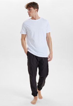 Hvid kortærmet t-shirt sat sammen med sorte cargo bukser med sidelommer og elastiske manchetter, båret barfodet på en neutral baggrund.