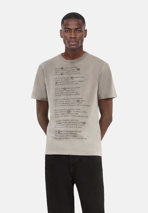 Gray cotton t-shirt with short sleeves, featuring printed poetic text in various fonts and sizes on the front. Worn with black striped pants.