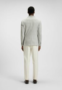 Szary w kratę żakiet z wykładanym kołnierzem, o średniej teksturze, w zestawieniu z białymi, dopasowanymi spodniami, noszony z ciemno-brązowymi butami. Widok z tyłu.