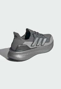 Grå atletiske sko med strikket overdel, tre kontrasterende striber og en tykk struktureret sål. Har "ULTRABOOST" branding på hælen.