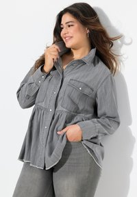 Camicia in denim grigio con design peplum, due tasche sul petto e orlo sfrangiato. Tessuto morbido, maniche lunghe e vestibilità rilassata.
