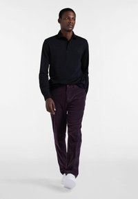 Schwarzes Langarm-Polohemd, lila Cordhosen, weiße Sneakers; elegantes Design, glatte Textur, dezentes Logo auf dem Hemd.