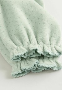 Blød, mintgrøn fleece cardigansweater med prikker, voluminøse manchetter og en tekstureret overflade, designet til varme og komfort.