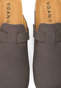 Gray vegan clogs with a smooth texture, open back, and a strap across the instep. Insoles feature brand name and size.
