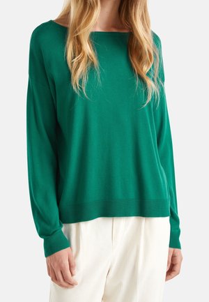 Grüner Pullover mit langen Ärmeln, weitem Ausschnitt und lockerem Schnitt, aus weichem Material gefertigt. Kombiniert mit hellen, strukturierten Hosen.