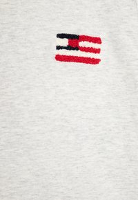 Grå bomulds t-shirt med et lille broderet flagdesign i rød, hvid og blå. Teksturen er blød med en glat overflade.