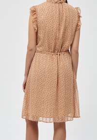 Světlé béžové šaty s květinovým vzorem, volánovými rukávy a stahovaným pasem. Pryžový materiál sahá těsně nad kolena, s zipovým zapínáním vzadu.