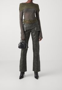 Olivgrön stickad topp med texturerade axlar, tillsammans med mörkgröna högmidjade byxor med metalldetaljer. Svart handväska och spetsiga stövlar.