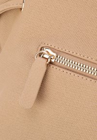 Borsa a tracolla in tessuto beige con texture, caratterizzata da una cerniera in metallo color oro e un pratico cursore liscio. Vista ravvicinata che mette in evidenza i materiali.