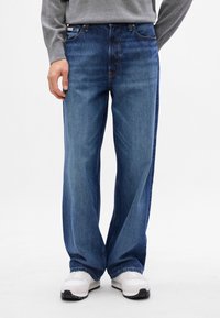 Jeans in denim blu a gamba larga con un classico design a cinque tasche e un leggero effetto usurato, abbinati a sneakers bianche.
