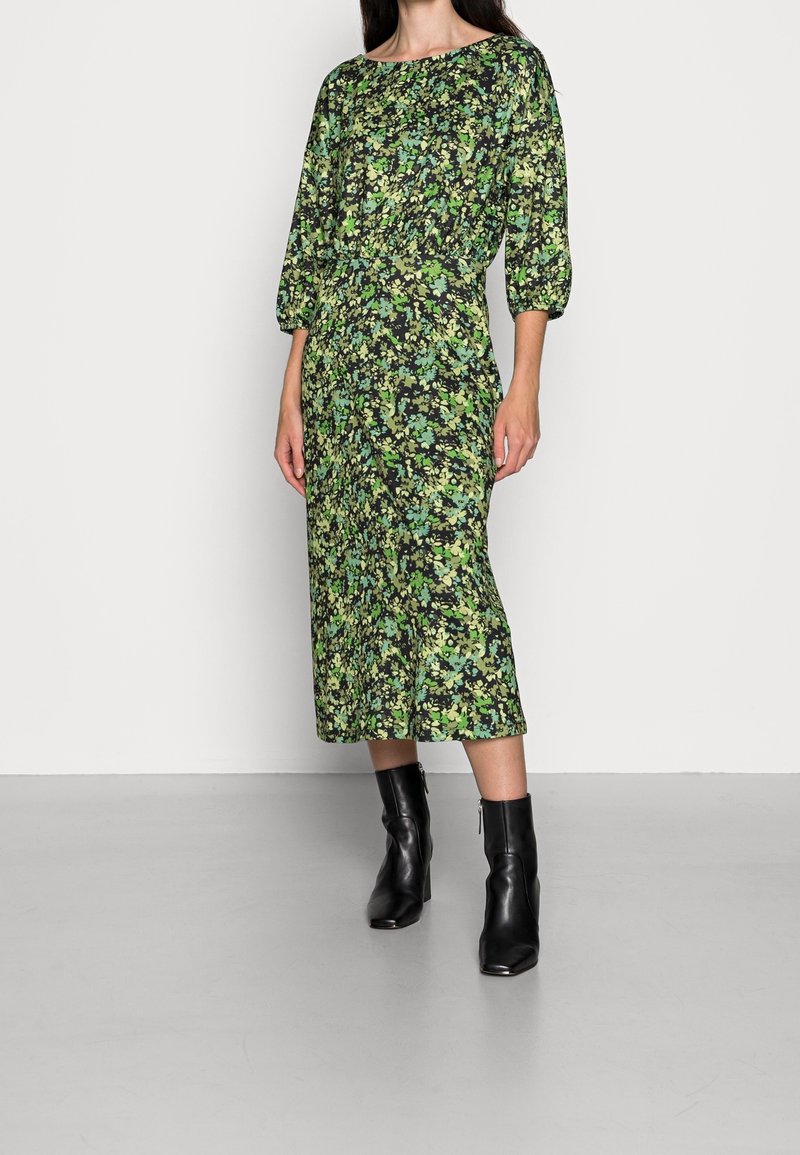 Vestido midi con estampado floral en tonos verdes, con escote barco y mangas abullonadas, combinado con botines negros. Textura suave.