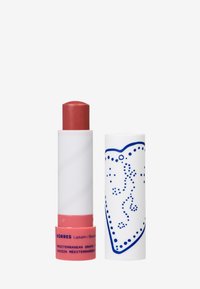 Bálsamo labial Korres en un tubo retráctil. El envase presenta un exterior blanco con patrones de puntos azules y una punta de bálsamo labial burdeos sólida.