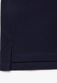 Détail de l'ourlet d'une chemise polo bleu marine, tissu texturé, évents latéraux et coutures visibles en bas. Design simple et classique.