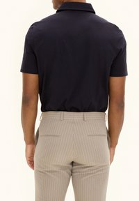 Navy polo shirt paired with striped beige trousers. Focus on the shirt's smooth texture and collar, with pleated details on the pants.