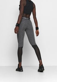 Grå atletiska leggings med svarta nätinsatser, utrustade med en märkeselastisk midja. Tyget har en melerad struktur.