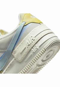 Gros plan d’un talon de basket blanc avec des accents jaunes et bleus et "AIR" embossé sur la semelle texturée.
