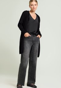 Cardigan largo negro, top de satén negro, vaqueros grises de pierna ancha. Textura suave, diseño casual, con bolsillos laterales y cintura ajustada. Zapatos planos negros.