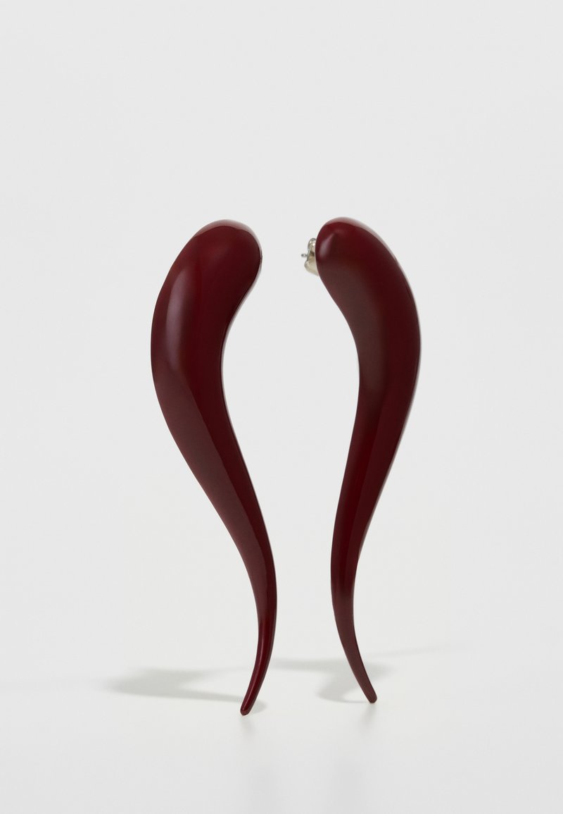 Punased, läikivad kõrvarõngad lainjalise, pikendatud kujuga, mis kitsenevad teravaks punktiks, ja neil on klamber kinnitamiseks.