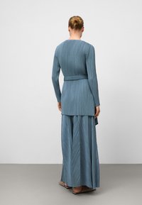 Długa, plisowana sukienka w teksturowanym, stonowanym niebieskim kolorze, z długimi rękawami i paskiem w talii, z warstwową spódnicą.