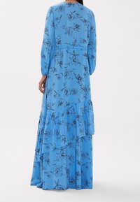 Robe longue bleue avec imprimé floral noir, volants, et manches longues. Tissu lisse, encolure ronde, détail de taille cintrée.