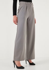 Grey wide-leg trousers made from smooth fabric, featuring a high waist, pleats, and two-button closure. Worn with black high heels.