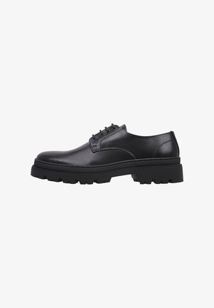 Zapato de vestir de cuero negro con cordones, suela gruesa y resistente y tacón bajo, mostrado de lado sobre fondo blanco.